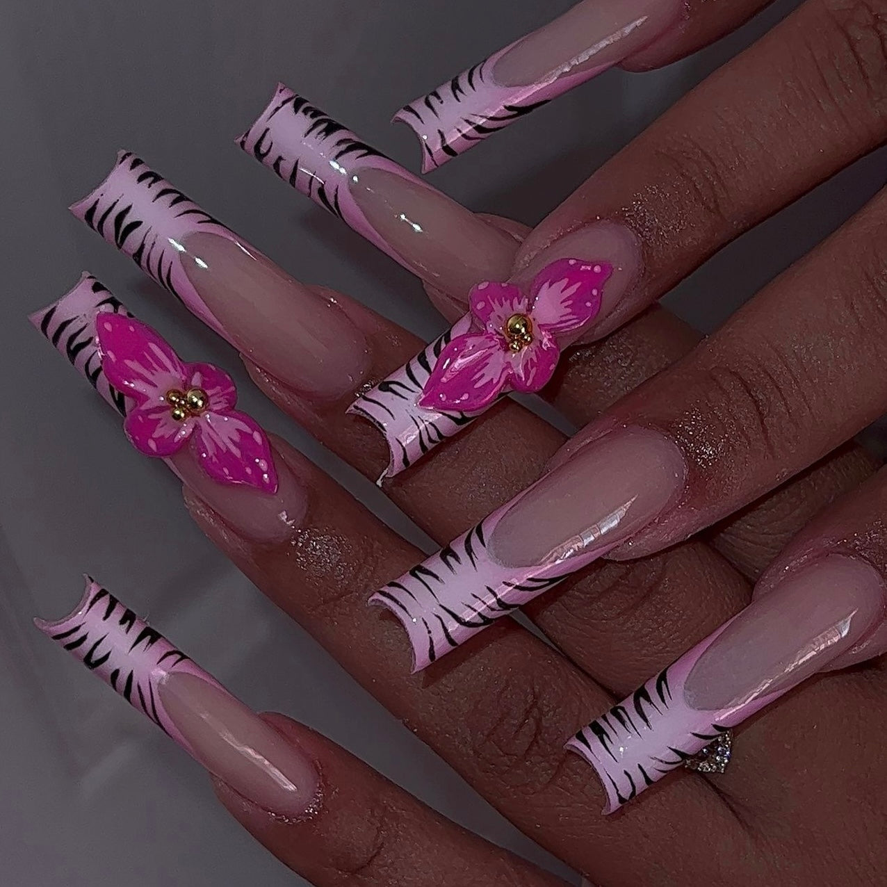 Zebra print French tip nails with floral accents, featuring zebra nail designs on a pink and white ombre base for a bold and elegant manicure.